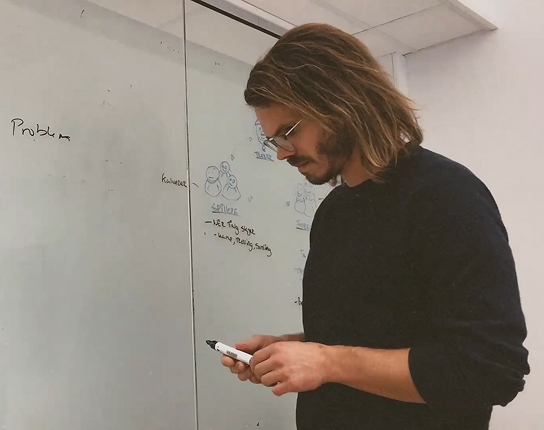 Designarbeid foran en whiteboard med skisser og problemstillinger